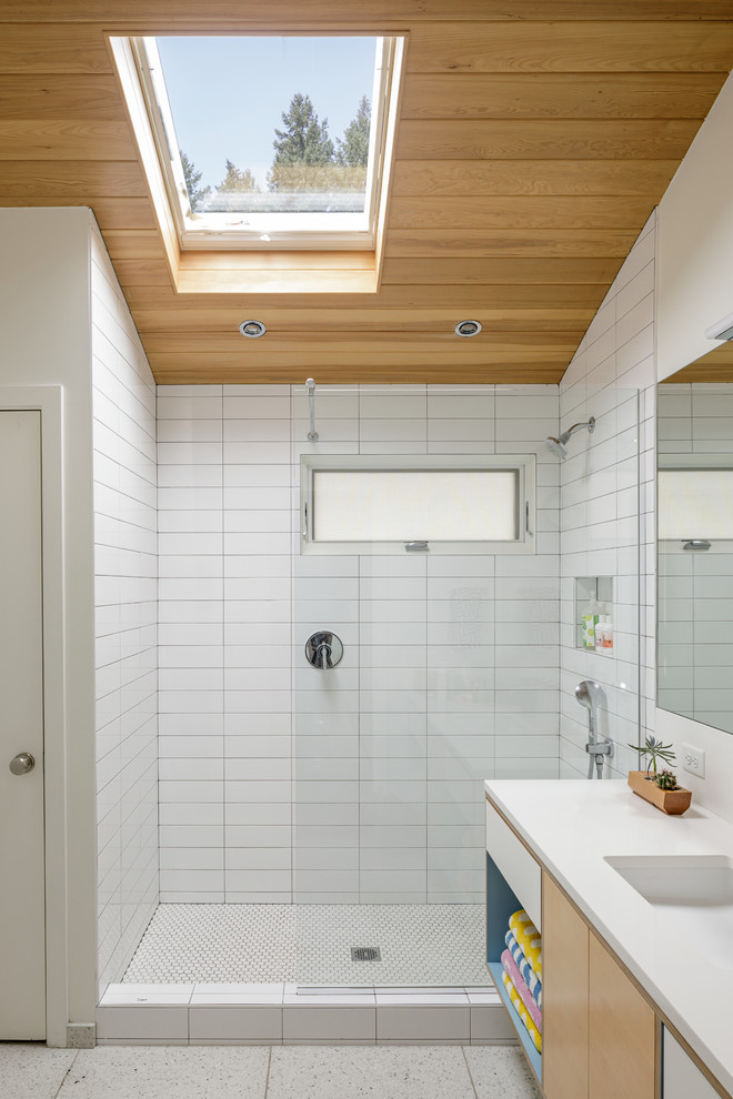 Cette photo montre une salle de bain rétro en bois clair avec un placard à porte plane, un plan de toilette blanc, un carrelage blanc, un mur blanc, un lavabo encastré, un sol blanc, aucune cabine et une fenêtre.