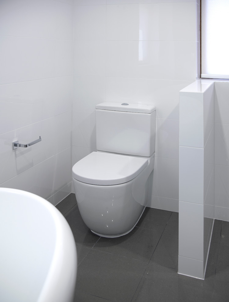 Photo of a medium sized contemporary ensuite bathroom in Other with an integrated sink, light wood cabinets, a freestanding bath, a walk-in shower, a wall mounted toilet, grey tiles, white walls and porcelain flooring.