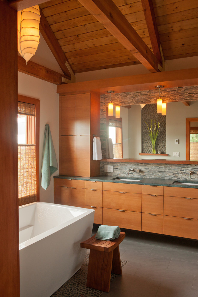 Идея дизайна: ванная комната в современном стиле с врезной раковиной, плоскими фасадами, фасадами цвета дерева среднего тона, отдельно стоящей ванной, серой плиткой, белыми стенами и окном