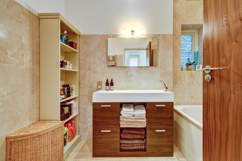 This is an example of a small contemporary family bathroom in London with flat-panel cabinets, dark wood cabinets, a built-in bath, a one-piece toilet, beige tiles, ceramic tiles, white walls, ceramic flooring, a built-in sink and solid surface worktops.