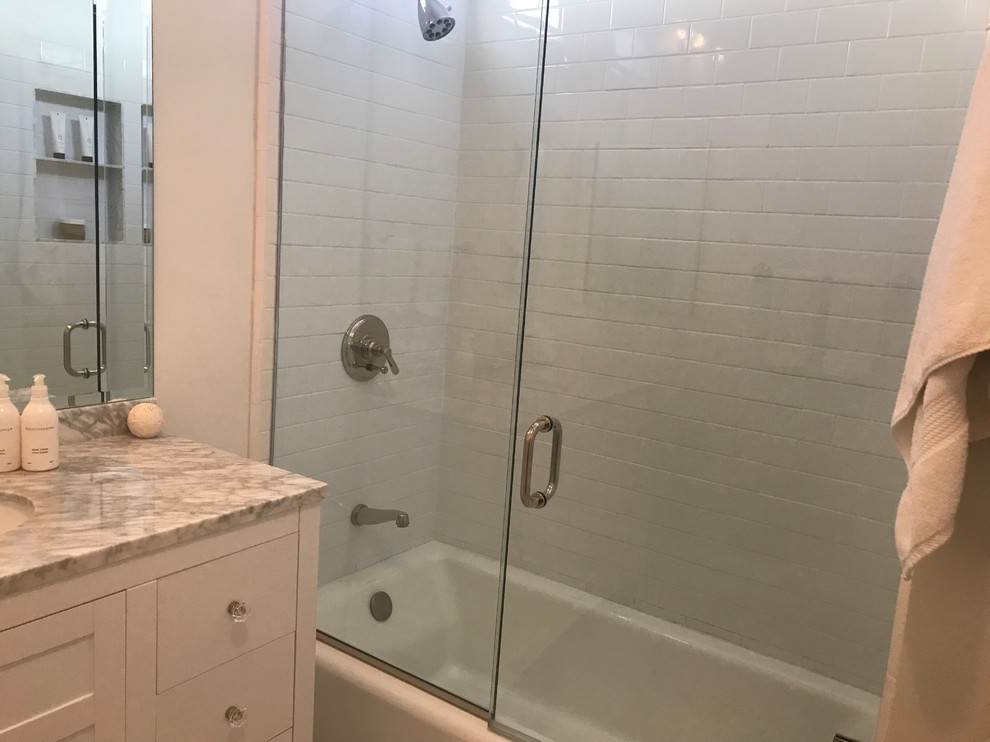 This is an example of a small classic ensuite bathroom in Los Angeles with flat-panel cabinets, white cabinets, an alcove bath, a shower/bath combination, a two-piece toilet, white tiles, metro tiles, white walls, marble flooring, a submerged sink, marble worktops, grey floors and a hinged door.