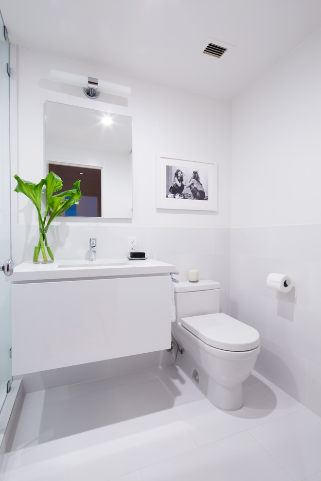 Modern inredning av ett mellanstort badrum med dusch, med ett undermonterad handfat, släta luckor, vita skåp, bänkskiva i kvarts, en toalettstol med hel cisternkåpa, vit kakel, porslinskakel, vita väggar och klinkergolv i porslin