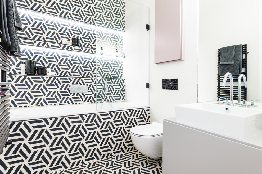 Inspiration for a medium sized eclectic bathroom in London with flat-panel cabinets, white cabinets, an alcove bath, a shower/bath combination, a wall mounted toilet, black and white tiles, white walls, a vessel sink, multi-coloured floors and white worktops.