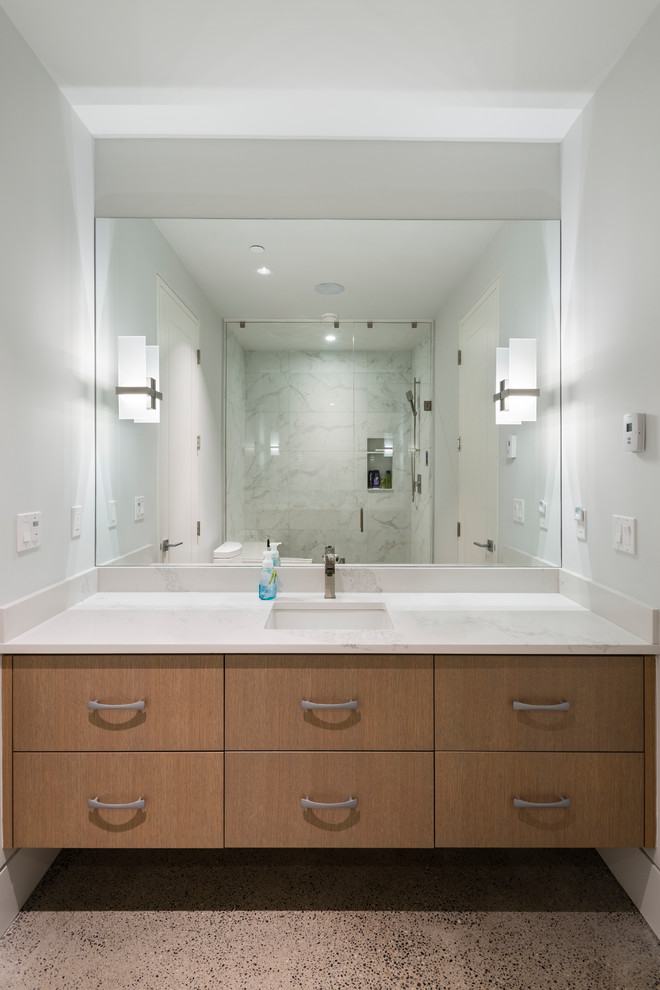Inspiration for a large transitional 3/4 concrete floor and gray floor alcove shower remodel in Vancouver with flat-panel cabinets, brown cabinets, a two-piece toilet, white walls, an undermount sink, marble countertops, a hinged shower door and white countertops