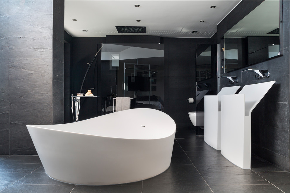 Cette image montre une salle de bain principale minimaliste avec une baignoire indépendante, une douche ouverte, WC suspendus, un carrelage noir, des carreaux de céramique, un mur noir, un plan vasque, un sol noir et aucune cabine.