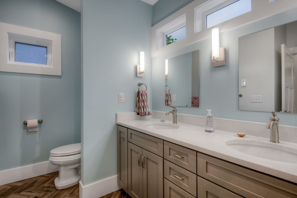 Aménagement d'une salle de bain principale moderne de taille moyenne avec un placard avec porte à panneau encastré, des portes de placard grises, un combiné douche/baignoire, un carrelage métro, un lavabo encastré, un plan de toilette en quartz, une baignoire posée, un carrelage gris, un mur bleu et un sol en bois brun.