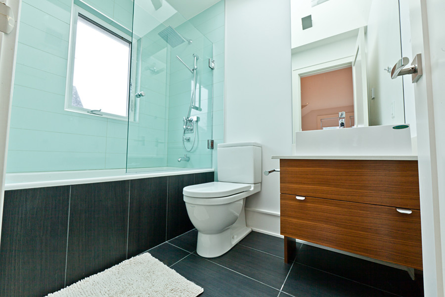 Idéer för att renovera ett litet funkis vit vitt badrum med dusch, med släta luckor, skåp i mörkt trä, ett badkar i en alkov, en dusch/badkar-kombination, en toalettstol med separat cisternkåpa, blå kakel, glaskakel, vita väggar, klinkergolv i porslin, ett fristående handfat, bänkskiva i akrylsten, svart golv och med dusch som är öppen