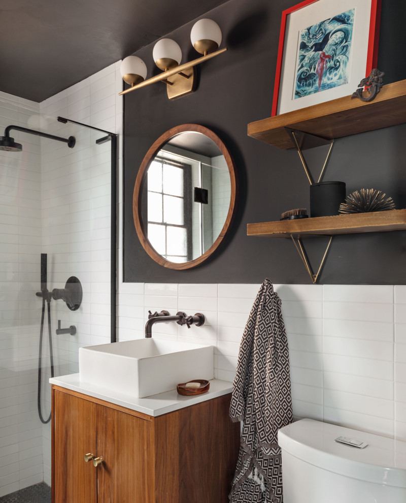 ニューヨークにあるトランジショナルスタイルのおしゃれなバスルーム (浴槽なし) (フラットパネル扉のキャビネット、中間色木目調キャビネット、白いタイル、黒い壁、ベッセル式洗面器、白い洗面カウンター) の写真