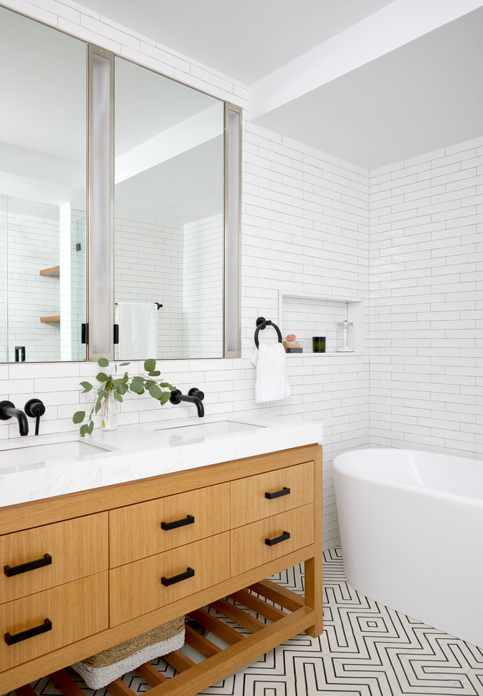 ニューヨークにあるコンテンポラリースタイルのおしゃれな浴室 (フラットパネル扉のキャビネット、中間色木目調キャビネット、置き型浴槽、白いタイル、白い壁、アンダーカウンター洗面器、マルチカラーの床、白い洗面カウンター) の写真