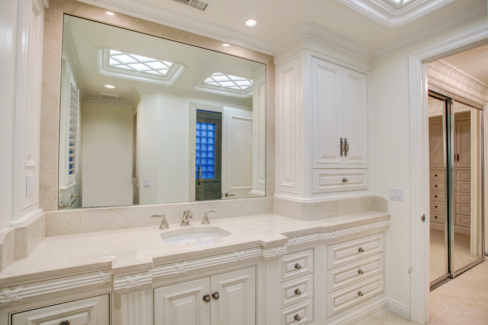 Bild på ett stort vintage en-suite badrum, med ett undermonterad handfat, luckor med profilerade fronter, vita skåp, marmorbänkskiva, ett undermonterat badkar, en hörndusch, en toalettstol med hel cisternkåpa, beige kakel, stenhäll, beige väggar och marmorgolv