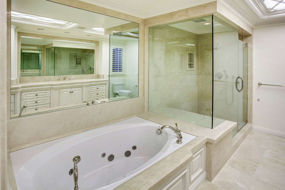 Cette image montre une grande salle de bain principale traditionnelle avec un lavabo encastré, un placard à porte affleurante, des portes de placard blanches, un plan de toilette en marbre, une baignoire encastrée, une douche d'angle, WC à poser, un carrelage beige, des dalles de pierre, un mur beige et un sol en marbre.