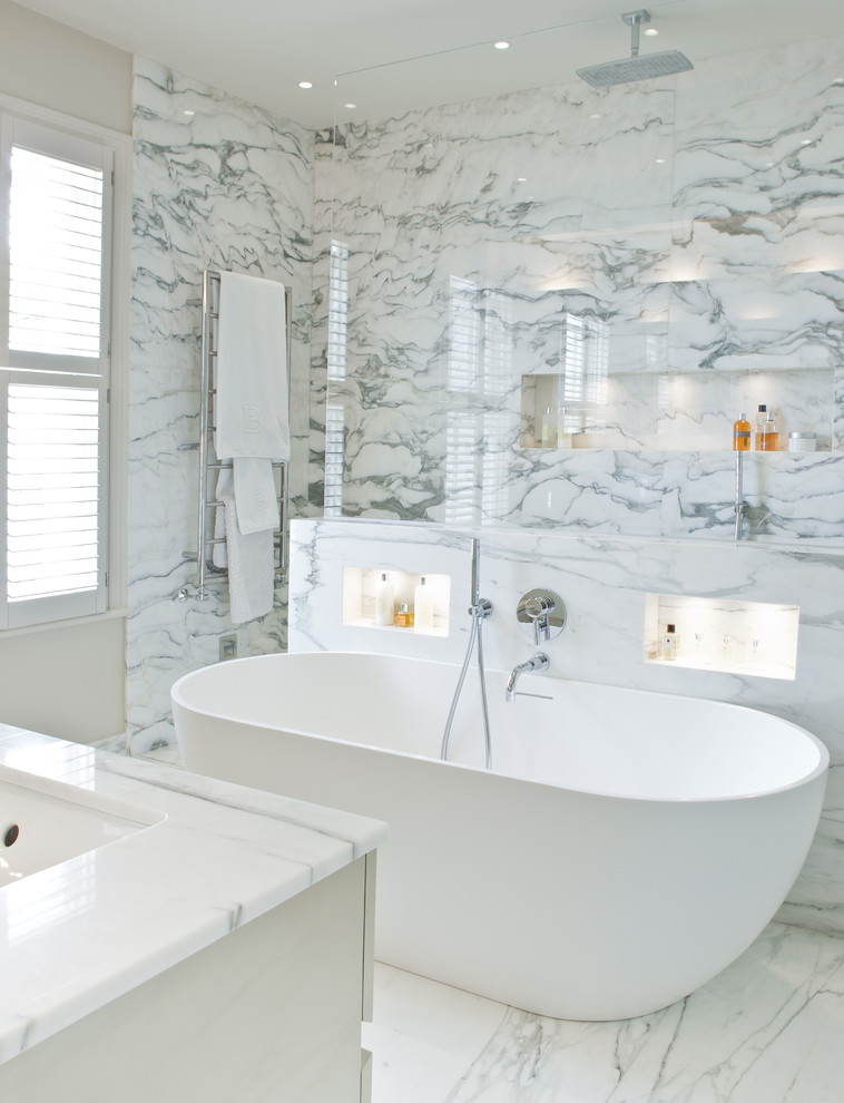 Inredning av ett klassiskt mellanstort badrum, med vita skåp, marmorbänkskiva, ett fristående badkar, vit kakel, vita väggar och marmorgolv