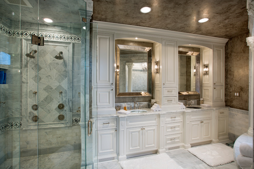 Cette image montre une grande salle de bain principale traditionnelle avec un lavabo encastré, un placard à porte affleurante, des portes de placard blanches, un plan de toilette en marbre, une baignoire en alcôve, une douche double, un carrelage gris, un carrelage de pierre, un mur gris et un sol en marbre.