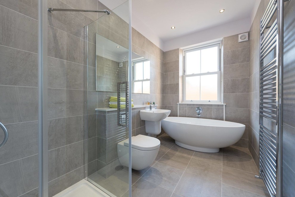 Modern inredning av ett mellanstort badrum, med luckor med upphöjd panel, grå skåp, ett fristående badkar, en öppen dusch, en vägghängd toalettstol, grå kakel, porslinskakel, vita väggar, klinkergolv i porslin, ett väggmonterat handfat och granitbänkskiva