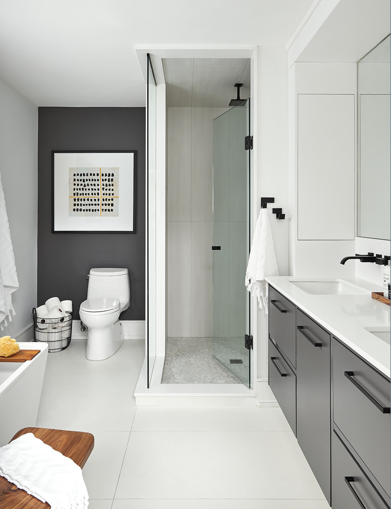 Inspiration for a medium sized contemporary ensuite bathroom in Toronto with flat-panel cabinets, grey cabinets, a freestanding bath, porcelain tiles, white walls, porcelain flooring, a submerged sink, engineered stone worktops, white floors, a hinged door and white worktops.