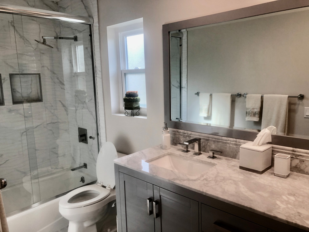 Traditional bathroom in Los Angeles with shaker cabinets, grey cabinets, an alcove bath, a shower/bath combination, a one-piece toilet, white tiles, marble tiles, grey walls, porcelain flooring, a submerged sink, marble worktops, grey floors, a sliding door and white worktops.