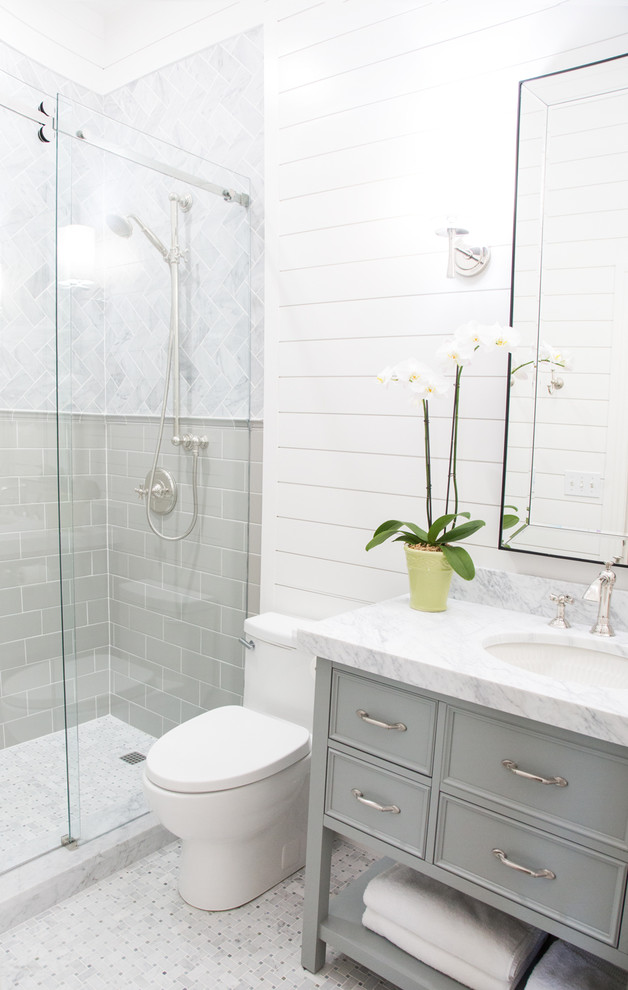 Foto på ett litet vintage badrum med dusch, med en toalettstol med hel cisternkåpa, marmorkakel, vita väggar, mosaikgolv, ett undermonterad handfat, marmorbänkskiva, grå skåp, en dusch i en alkov, grå kakel, grått golv, dusch med skjutdörr och luckor med infälld panel