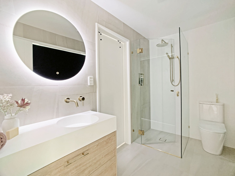 Стильный дизайн: маленькая ванная комната в стиле модернизм с фасадами в стиле шейкер, фасадами цвета дерева среднего тона, угловым душем, раздельным унитазом, серой плиткой, керамогранитной плиткой, белыми стенами, полом из керамогранита, душевой кабиной, монолитной раковиной, столешницей из искусственного камня, серым полом, душем с распашными дверями, белой столешницей, нишей, тумбой под одну раковину и напольной тумбой для на участке и в саду - последний тренд