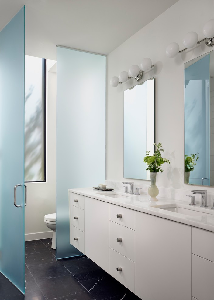 Foto de cuarto de baño contemporáneo con armarios con paneles lisos, puertas de armario blancas, paredes blancas, lavabo bajoencimera, suelo negro y espejo con luz