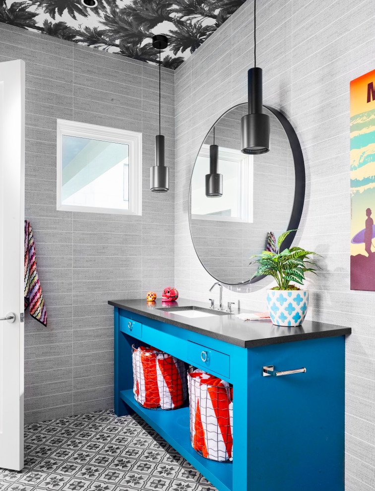 Mid-sized beach style 3/4 gray tile ceramic tile, gray floor and single-sink bathroom photo in Austin with open cabinets, blue cabinets, gray walls, a drop-in sink, black countertops and a built-in vanity