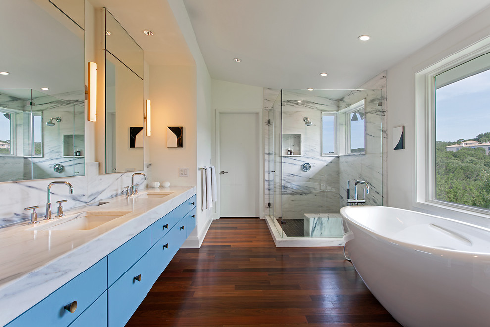Large contemporary ensuite bathroom in Austin with a submerged sink, flat-panel cabinets, blue cabinets, a freestanding bath, a corner shower, white walls, dark hardwood flooring, marble worktops, brown floors and a hinged door.
