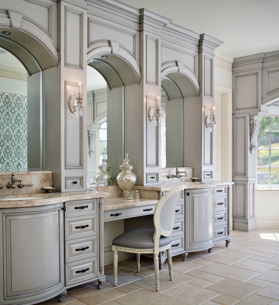 Inredning av ett klassiskt badrum, med ett undermonterad handfat, grå skåp, marmorbänkskiva, ett fristående badkar, grå kakel, stenkakel och luckor med upphöjd panel