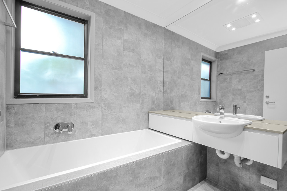 Modernes Badezimmer mit flächenbündigen Schrankfronten, weißen Schränken, Einbaubadewanne, grauen Fliesen, Wandwaschbecken, grauem Boden, grauer Waschtischplatte, Einzelwaschbecken und schwebendem Waschtisch in Sydney