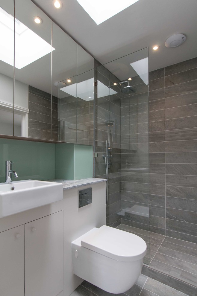 ロンドンにあるお手頃価格の小さなコンテンポラリースタイルのおしゃれな浴室 (壁付け型シンク、フラットパネル扉のキャビネット、グレーのキャビネット、珪岩の洗面台、ドロップイン型浴槽、オープン型シャワー、一体型トイレ	、グレーのタイル、セラミックタイル、グレーの壁、セラミックタイルの床) の写真