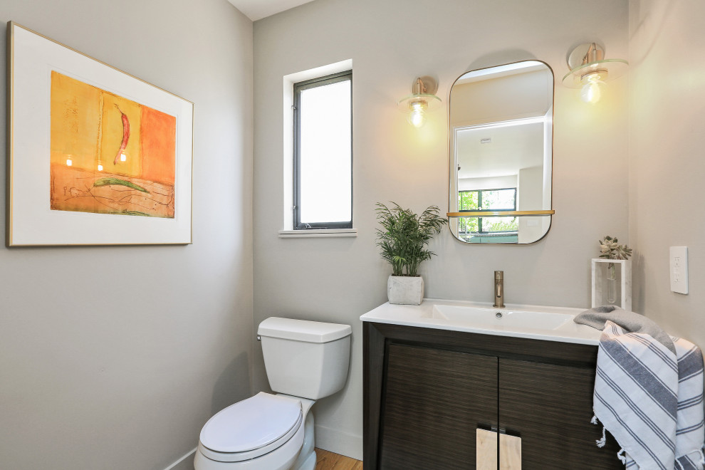 Design ideas for a small contemporary bathroom in San Francisco with freestanding cabinets, dark wood cabinets, a two-piece toilet, beige walls, light hardwood flooring, an integrated sink, solid surface worktops, white worktops, a single sink and a freestanding vanity unit.