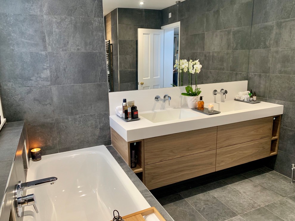 Inspiration for a large modern master gray tile and porcelain tile porcelain tile and gray floor bathroom remodel in Other with flat-panel cabinets, medium tone wood cabinets, a wall-mount toilet, gray walls, an integrated sink, solid surface countertops and white countertops