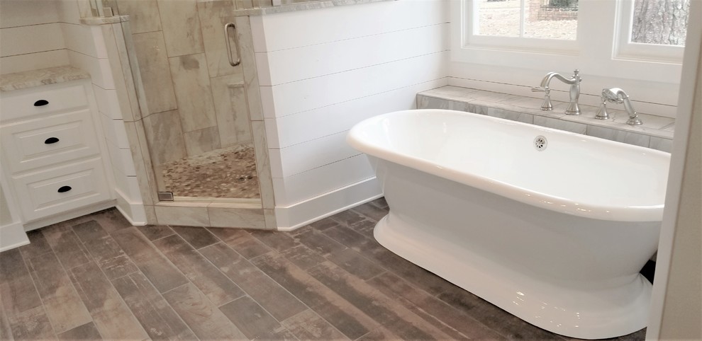 This is an example of a large rural ensuite bathroom in Other with shaker cabinets, white cabinets, a freestanding bath, a corner shower, multi-coloured tiles, porcelain tiles, grey walls, porcelain flooring, quartz worktops, brown floors, a hinged door and white worktops.