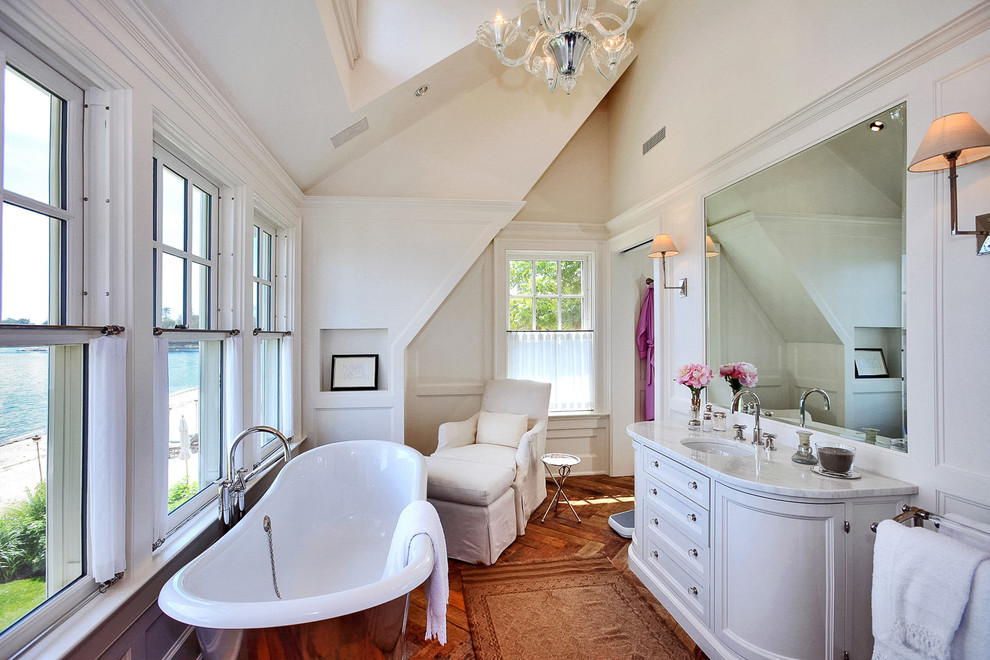 ニューヨークにあるトラディショナルスタイルのおしゃれな浴室 (アンダーカウンター洗面器、落し込みパネル扉のキャビネット、置き型浴槽、ベージュの壁、無垢フローリング、白いキャビネット) の写真