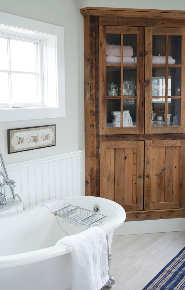 Réalisation d'une salle de bain principale champêtre en bois brun avec un placard à porte vitrée, une baignoire sur pieds, un mur vert, un sol en carrelage de porcelaine et un sol beige.