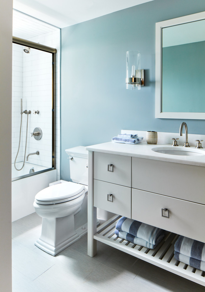 На фото: маленькая ванная комната в стиле неоклассика (современная классика) с плоскими фасадами, серыми фасадами, ванной в нише, раздельным унитазом, белой плиткой, синими стенами, полом из керамогранита, врезной раковиной, серым полом, белой столешницей, тумбой под одну раковину, напольной тумбой, душем над ванной и душем с раздвижными дверями для на участке и в саду с