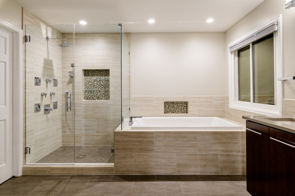 Cette image montre une grande salle de bain principale design en bois foncé avec un placard à porte plane, une baignoire d'angle, une douche d'angle, un carrelage beige, des carreaux de porcelaine, un mur beige, un sol en vinyl, un lavabo encastré, un plan de toilette en carrelage, un sol beige et une cabine de douche à porte battante.