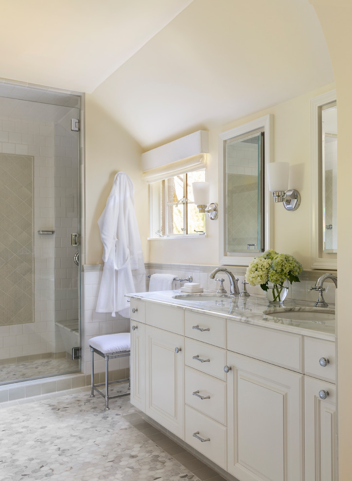 Elegant white tile marble floor and white floor alcove shower photo in Los Angeles with raised-panel cabinets, white cabinets, yellow walls, an undermount sink, marble countertops and a hinged shower door