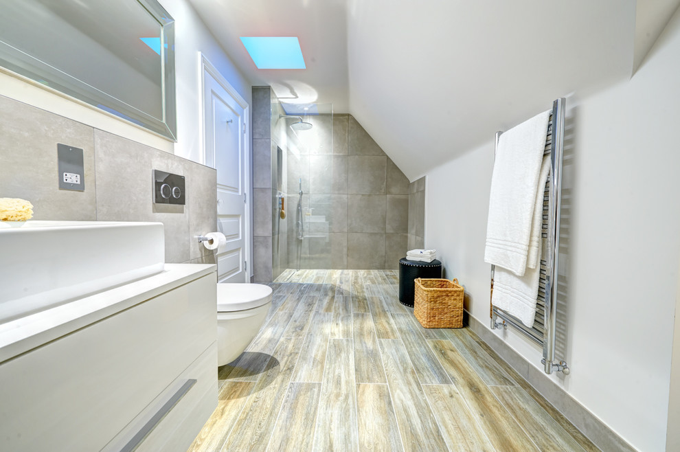 This is an example of a large contemporary ensuite bathroom in London with white cabinets, a walk-in shower, a wall mounted toilet, porcelain tiles, grey walls, porcelain flooring, a trough sink, flat-panel cabinets and multi-coloured tiles.