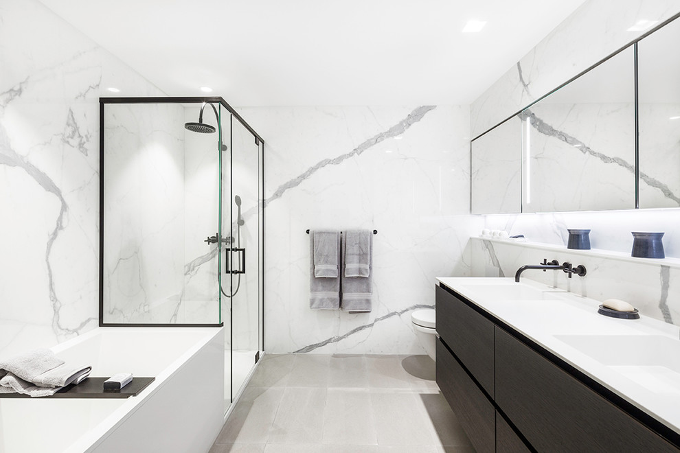 Modernes Badezimmer mit flächenbündigen Schrankfronten, dunklen Holzschränken, weißen Fliesen, Steinplatten, integriertem Waschbecken und Falttür-Duschabtrennung in Montreal