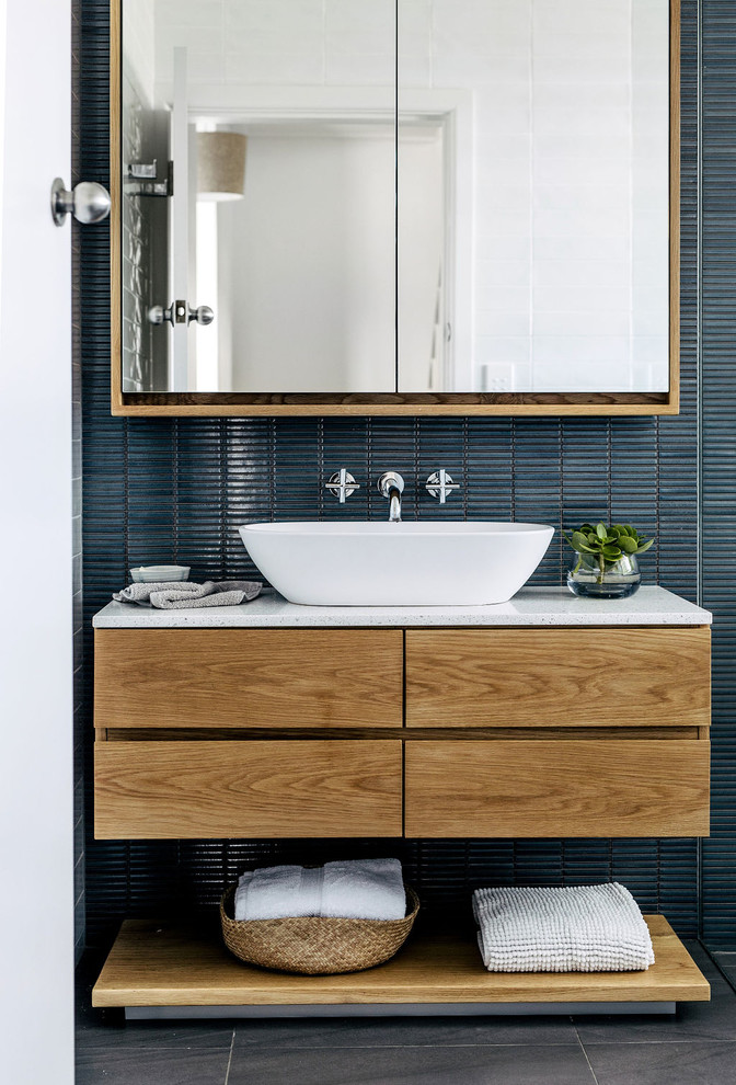 Идея дизайна: ванная комната в современном стиле с плоскими фасадами, фасадами цвета дерева среднего тона, синей плиткой, плиткой мозаикой, синими стенами, настольной раковиной, серым полом и белой столешницей