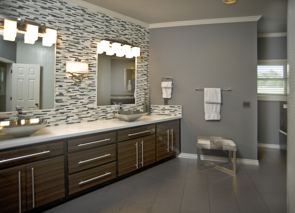 Cette image montre une salle de bain principale design en bois foncé avec une vasque, un placard à porte plane, un plan de toilette en surface solide, une baignoire posée, un carrelage gris, des carreaux de porcelaine, un mur gris et un sol en carrelage de porcelaine.