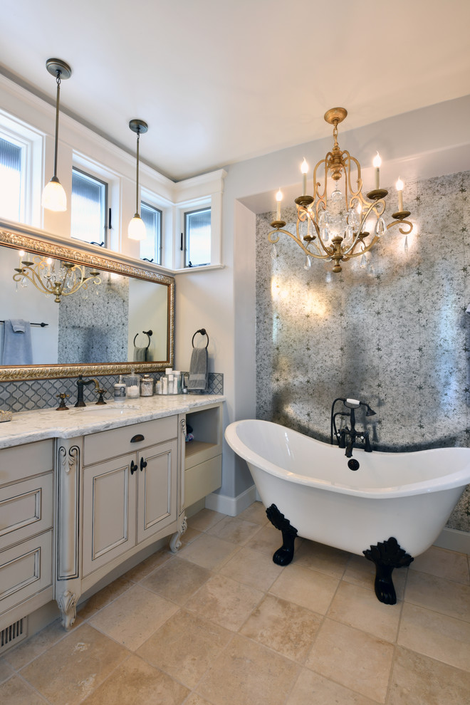Cette image montre une salle de bain principale style shabby chic avec un placard avec porte à panneau encastré, des portes de placard grises, une baignoire sur pieds, un carrelage gris, un mur gris, un lavabo encastré, un sol beige et un plan de toilette blanc.