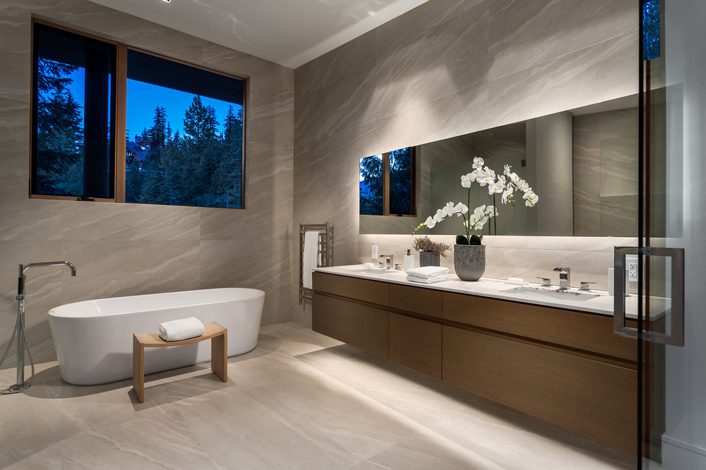 Cette photo montre une salle de bain tendance en bois foncé avec un lavabo encastré, un placard à porte plane, une baignoire indépendante et un carrelage gris.