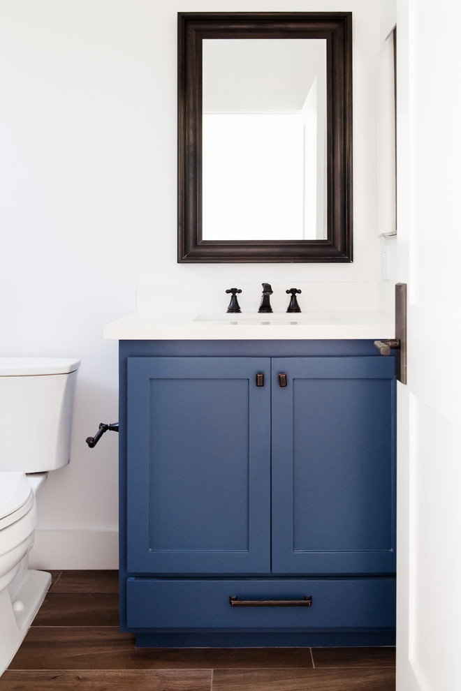 Exempel på ett mellanstort klassiskt vit vitt badrum med dusch, med en dusch i en alkov, en toalettstol med separat cisternkåpa, vita väggar, mörkt trägolv, ett undermonterad handfat, brunt golv, skåp i shakerstil, blå skåp, vit kakel, tunnelbanekakel och bänkskiva i akrylsten