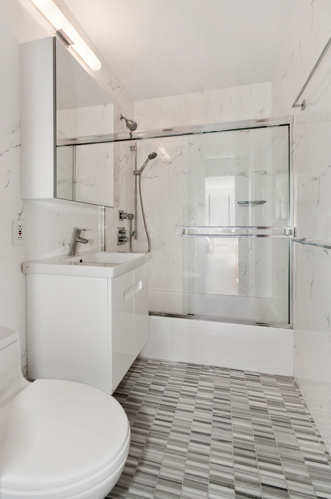 Example of a small trendy kids' white tile and porcelain tile porcelain tile and gray floor bathroom design in New York with flat-panel cabinets, white cabinets, a one-piece toilet, white walls, solid surface countertops, a drop-in sink and white countertops
