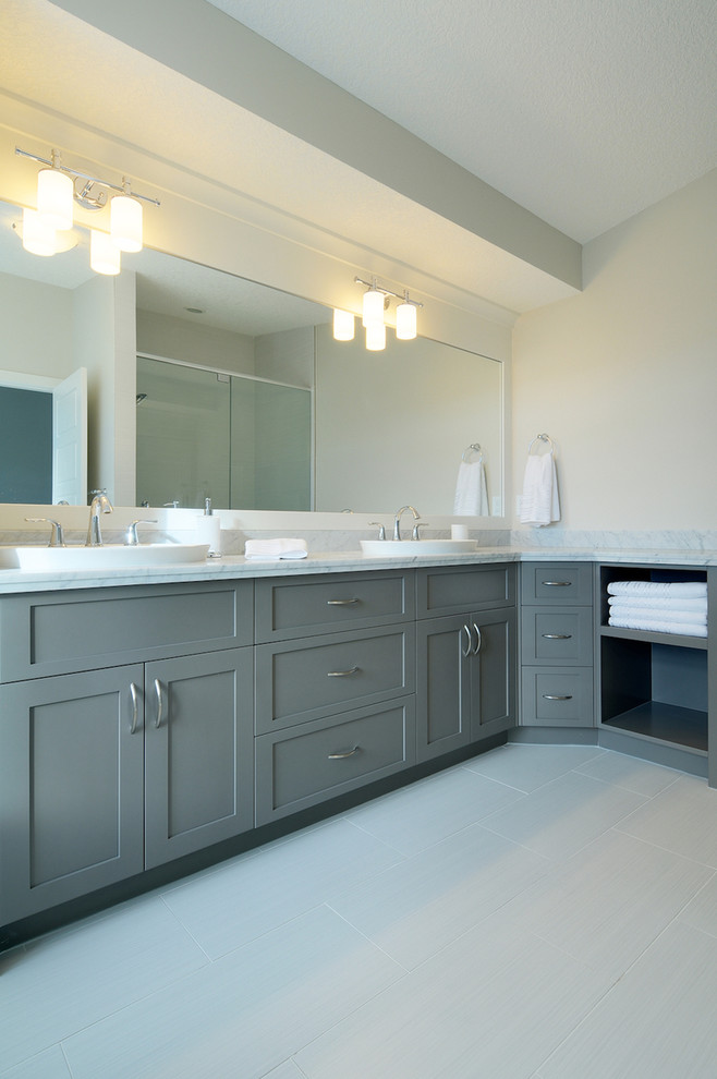 Diseño de cuarto de baño actual con lavabo sobreencimera, armarios estilo shaker, puertas de armario grises y baldosas y/o azulejos grises