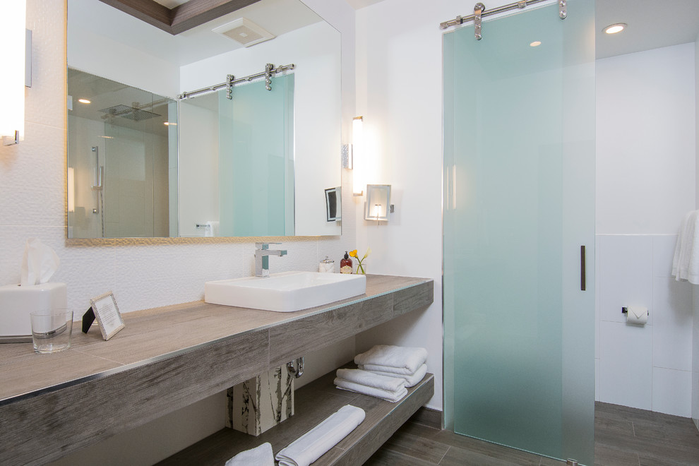 Foto på ett stort funkis en-suite badrum, med ett fristående handfat, kaklad bänkskiva, en dusch i en alkov, en vägghängd toalettstol, brun kakel, keramikplattor, vita väggar och klinkergolv i keramik