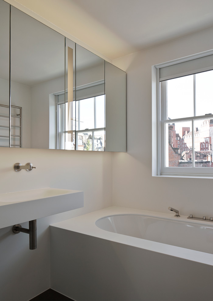 Idee per una piccola stanza da bagno padronale minimal con ante di vetro, ante bianche, top in superficie solida, vasca da incasso, lavabo sospeso, pareti bianche e pavimento in cemento