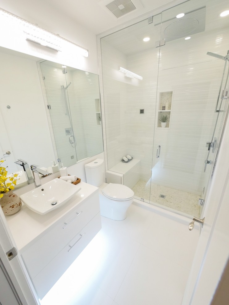 Bild på ett mellanstort funkis badrum med dusch, med släta luckor, vita skåp, en dusch i en alkov, en toalettstol med hel cisternkåpa, vit kakel, porslinskakel, vita väggar, klinkergolv i porslin, ett fristående handfat, bänkskiva i kvarts, vitt golv och dusch med gångjärnsdörr