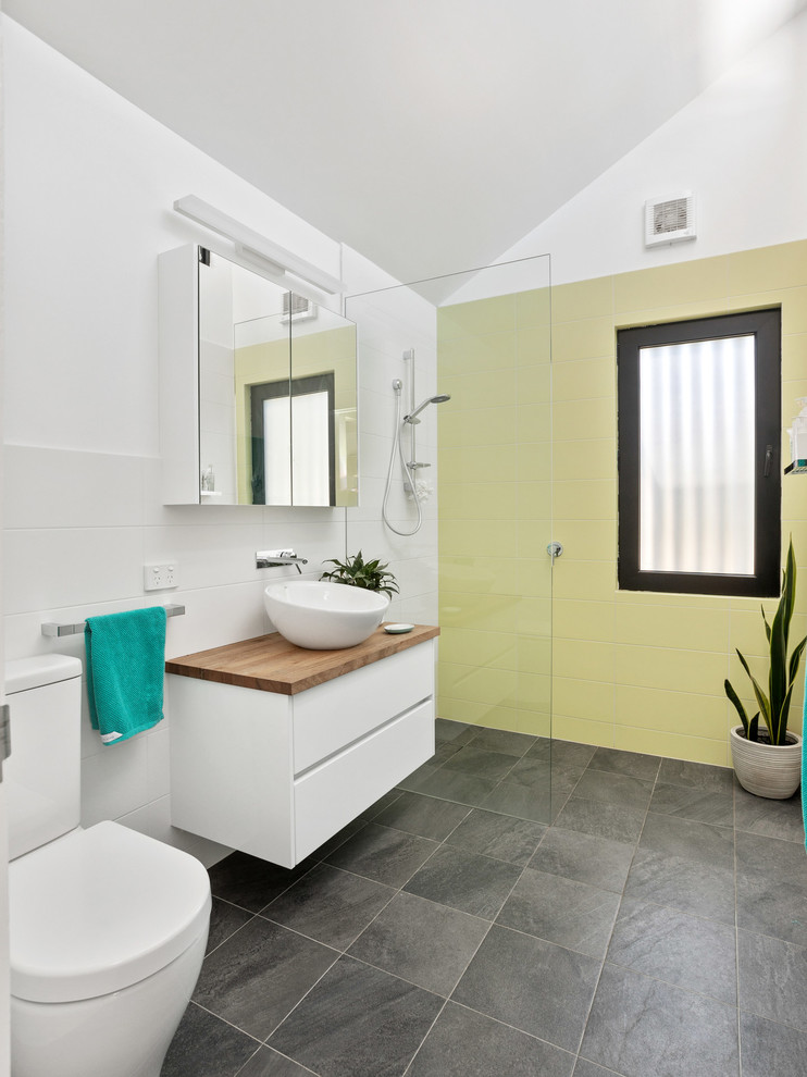 На фото: ванная комната в современном стиле с плоскими фасадами, белыми фасадами, душем без бортиков, раздельным унитазом, желтой плиткой, белыми стенами, душевой кабиной, настольной раковиной, столешницей из дерева, серым полом, открытым душем и коричневой столешницей
