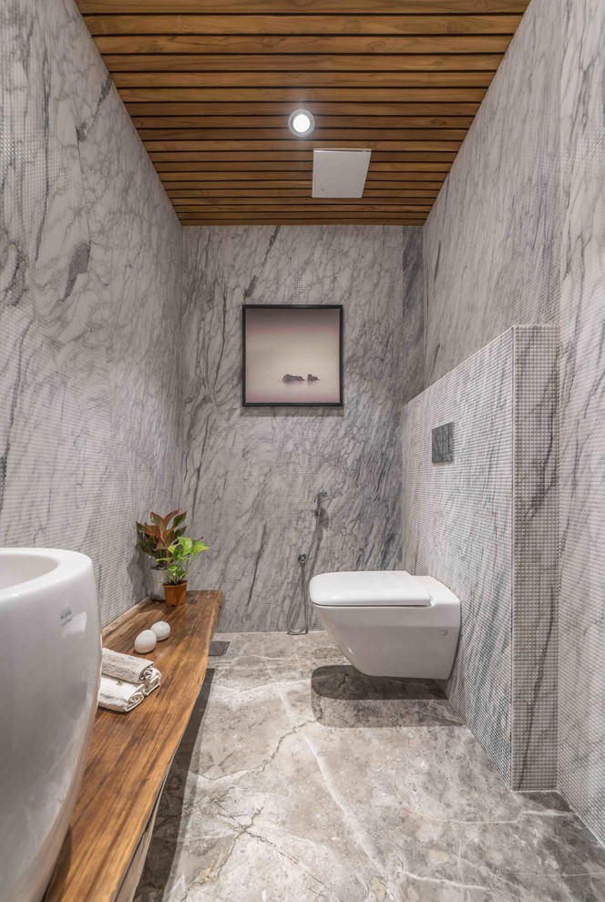 Modernes Badezimmer mit Wandtoilette, grauen Fliesen, Steinplatten, grauer Wandfarbe, Aufsatzwaschbecken, Waschtisch aus Holz, braunem Boden und brauner Waschtischplatte in Hyderabad